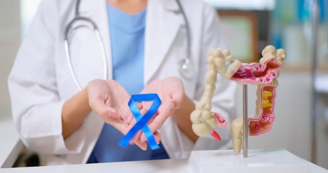 A female doctor is holding a blue ribbon in her hand for Colon Cancer- Screening Prevention and Treatment Month